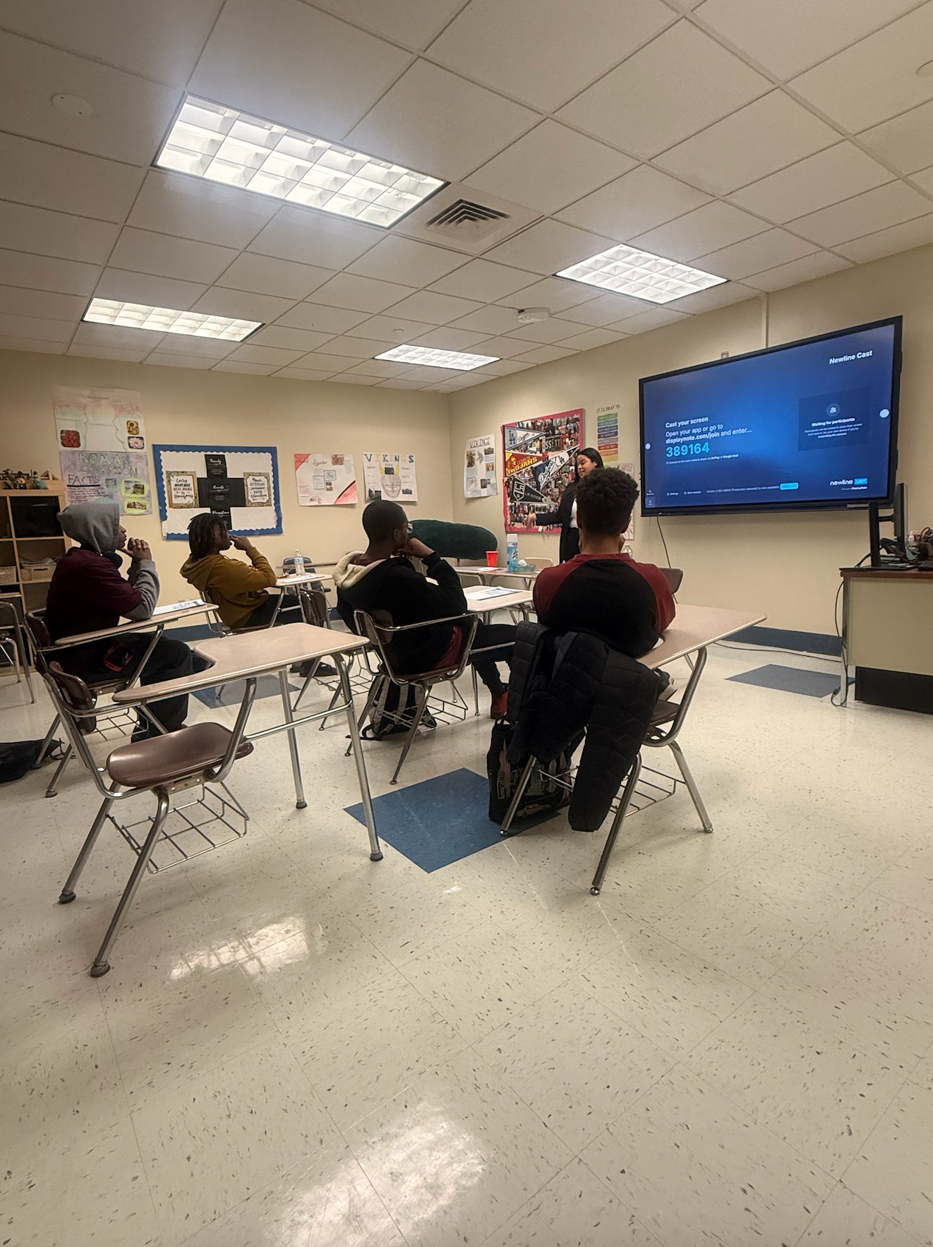 A presenter speaking to seated students in front of a classroom display