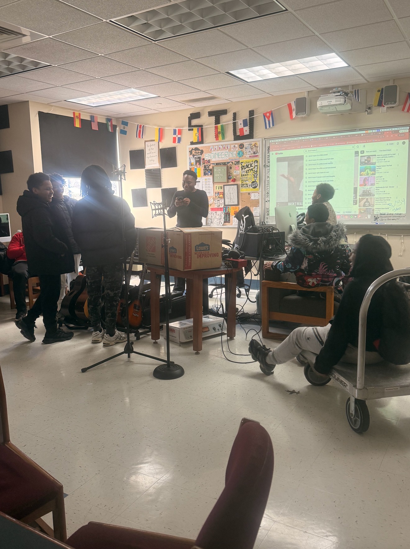Students gathered in a music studio with microphones, guitars, and a projector screen